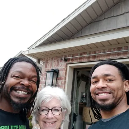 Two moving team members and a woman smiling outside a home