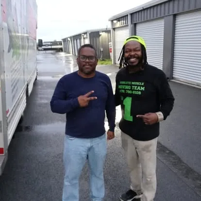 Two men beside a moving truck and storage units